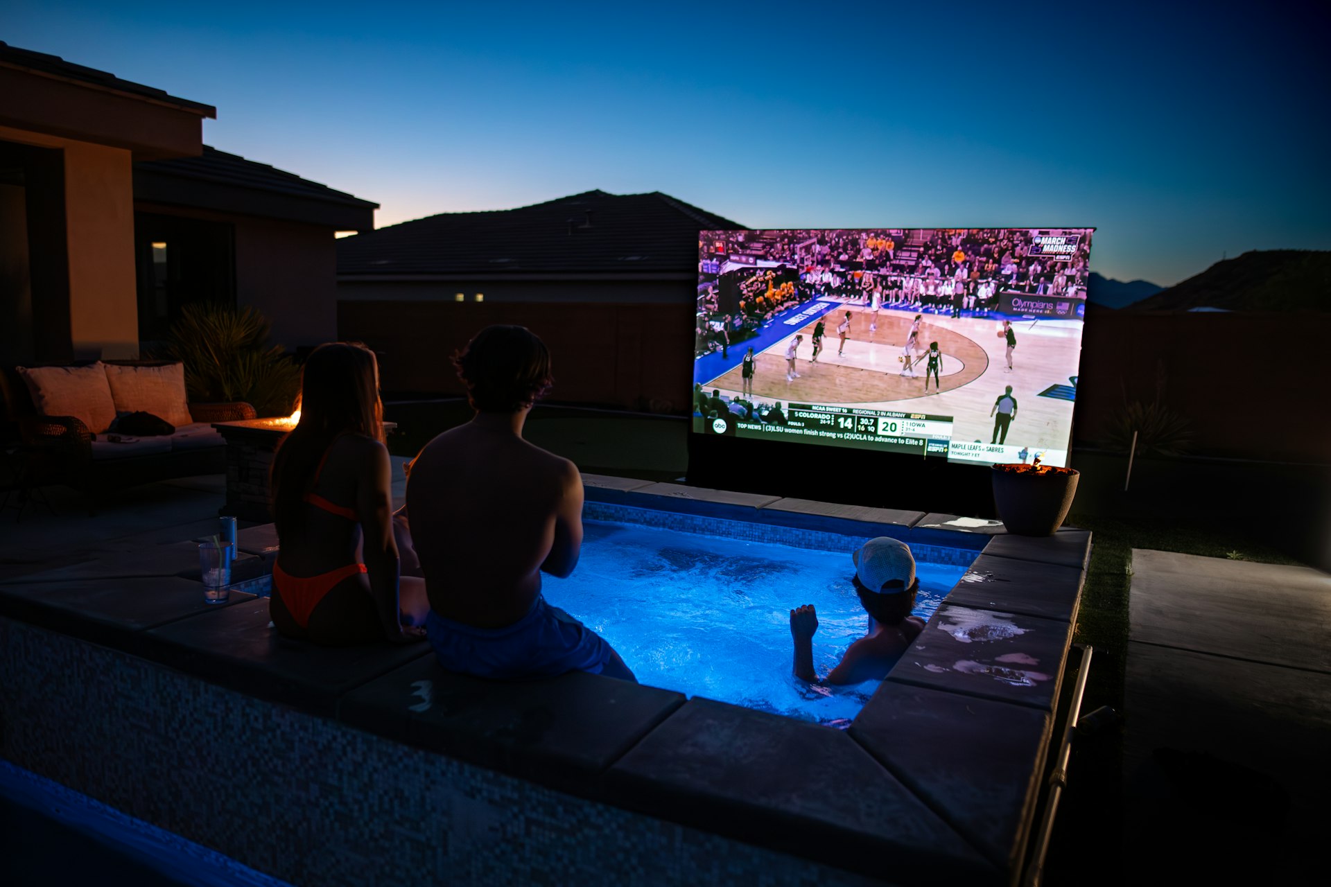 A group of people watching a game on a big screen outdoor TV